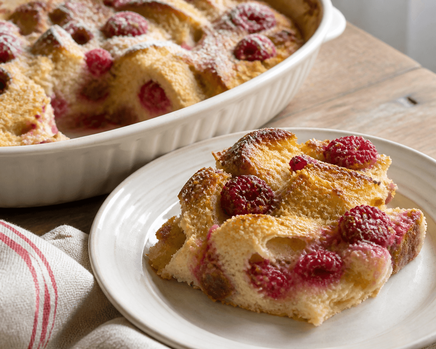 Pudding de pain doré aux framboises et vanille servi en part généreuse.